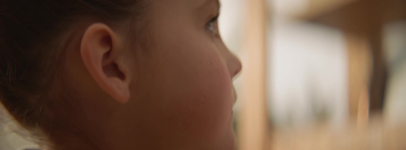 A boy is looking up from what he is doing as he sits inside in daylight