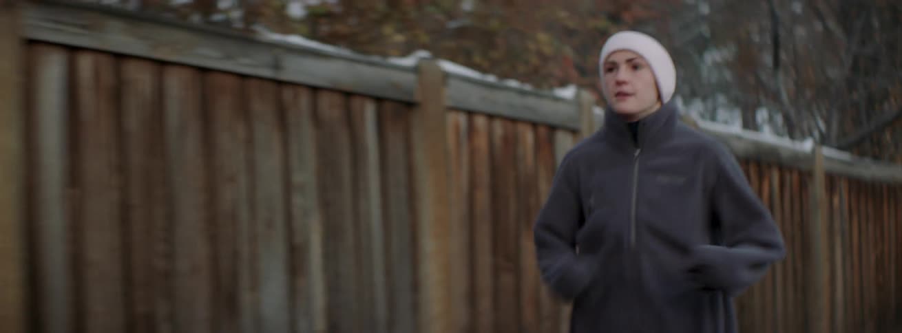 The woman is running past the wooden fence