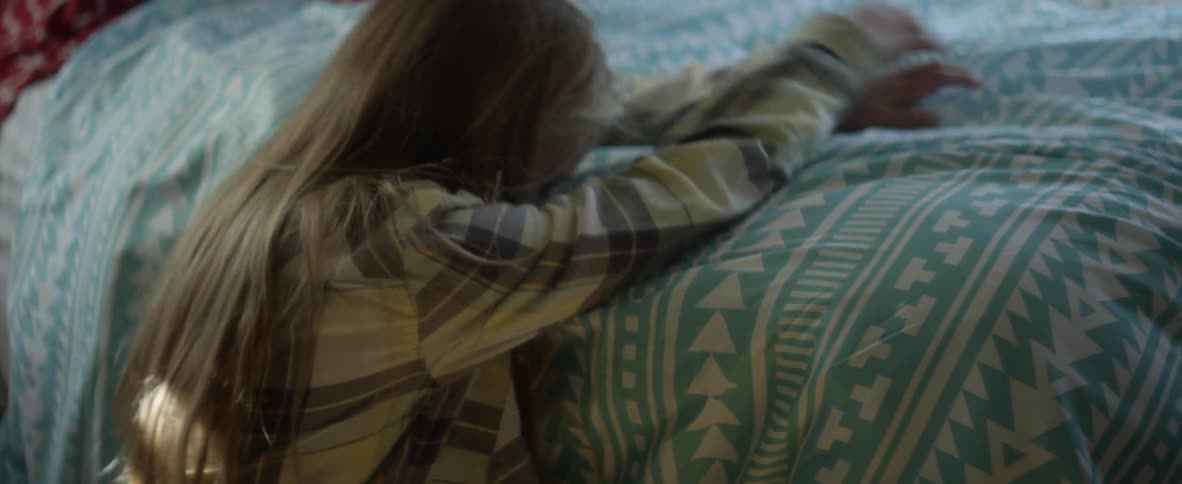A girl lays on a bedroom floor and pulls a blanket over her head