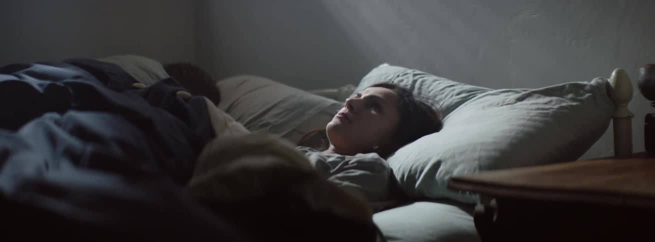 The woman lays awake in the bed near a sleeping man