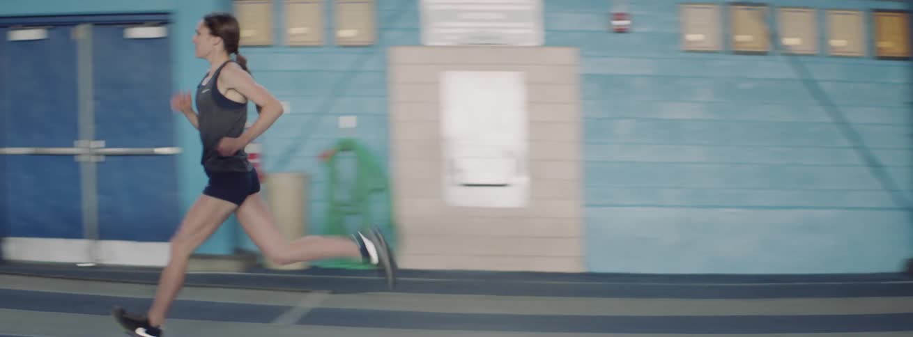 Woman runs on an indoor track as her coach encourages her
