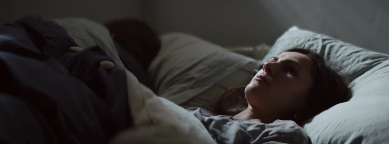 A woman lays awake in bed next to a man