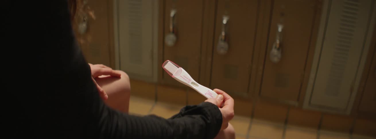 A woman is sitting in a locker-room holding at a pregnancy test