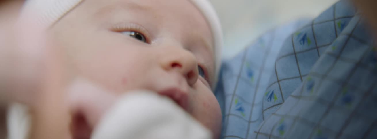 A baby moves his hands around in a person's arms