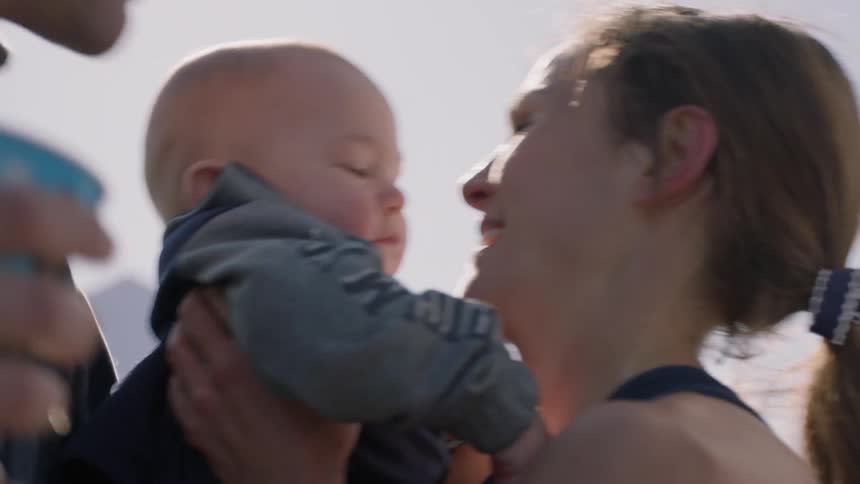 The man hands off a baby to a woman, then kisses her cheek