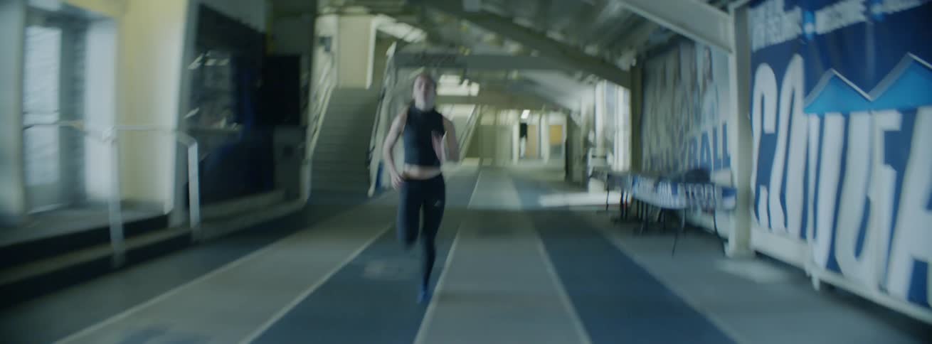 A female athlete is running a sprint on an indoor track during the day