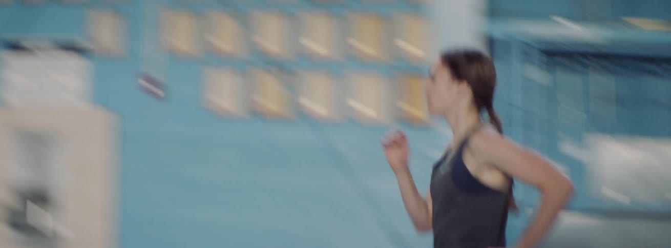 Woman runs on an indoor track as her coach encourages her