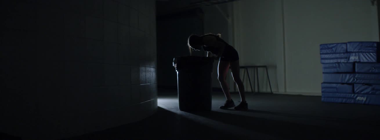 A woman in workout gear leans against a barrel and throws up