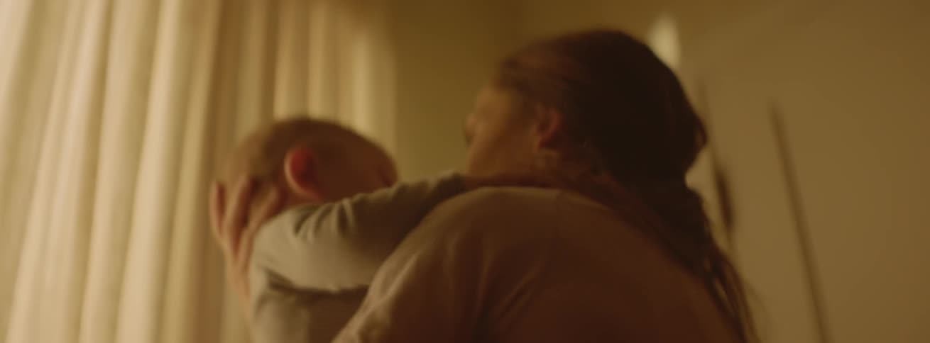 A woman is rocking and comforting her baby as she stands inside in daylight