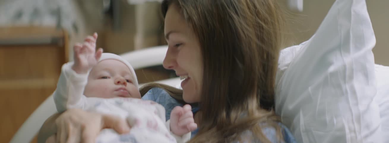 A doctor gives a newborn to a mother in bed