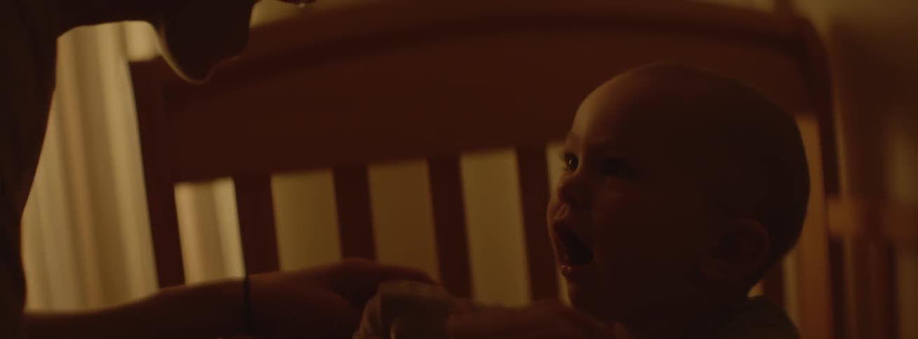 A woman is playing with her baby as it bounces in its crib in the morning