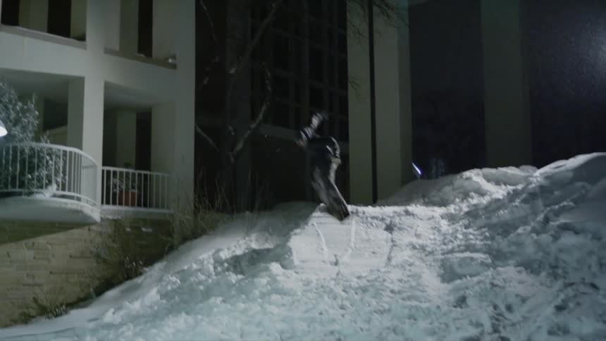 A snowboarder is jumping from a balcony onto a snowdrift at night