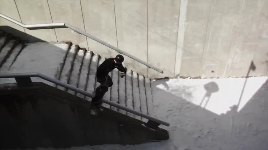 A young man grinds a stair rail with a snowboard