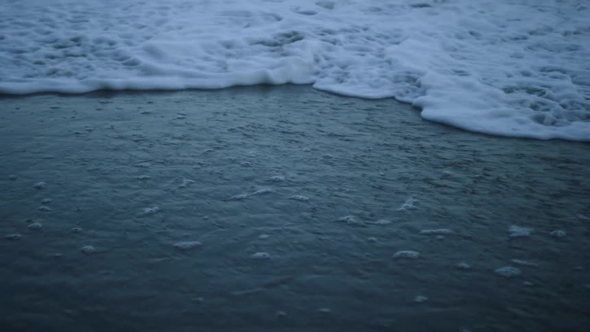 A wave is rolling onto a beach at dusk