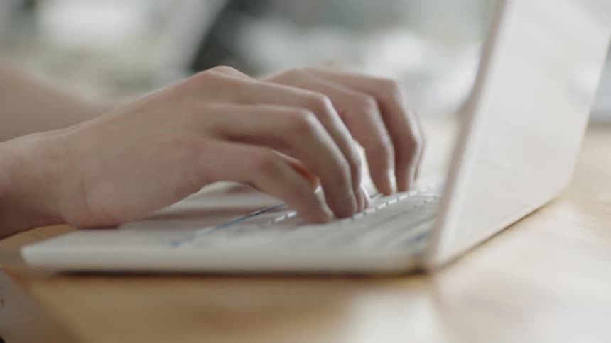 A person is typing on a white laptop