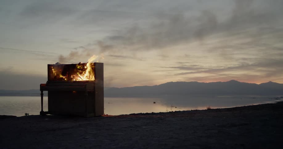 A piano is burning as it stands outside in a coastal area at dusk