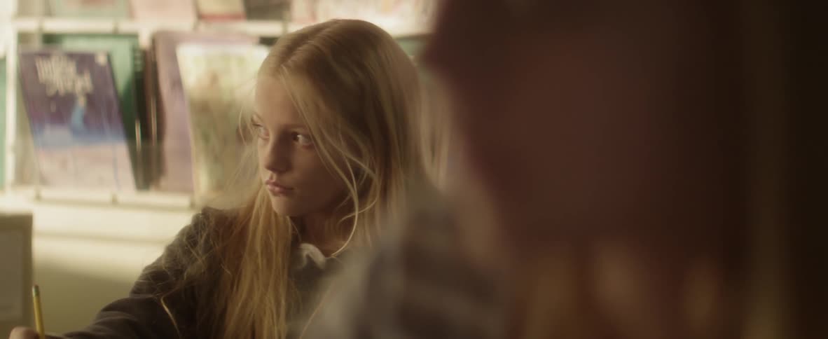 A teenage girl sitting writing with a pencil looking bored gets distracted momentarily
