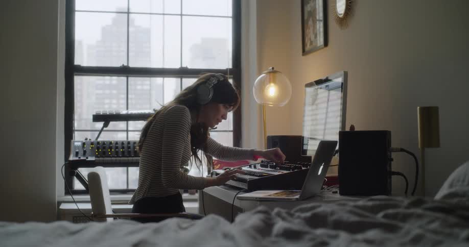 A woman plays the keyboard by a laptop