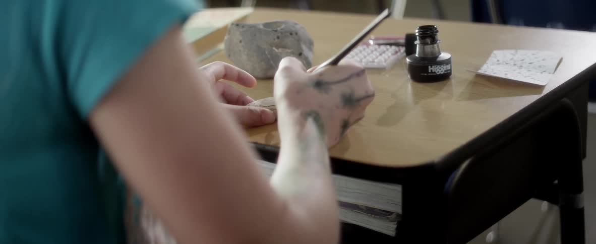 Woman painting a rock over a desk with her hand stained with ink