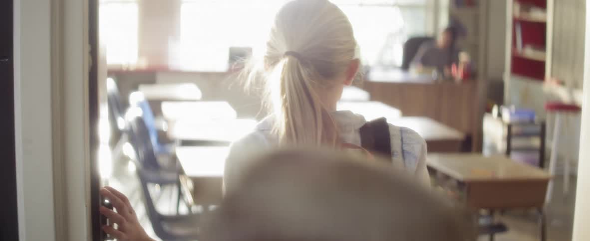 Children gathering their backpacks and leaving a classroom with one blonde girl stopping in front of an empty room and then turning to run back down the hallway