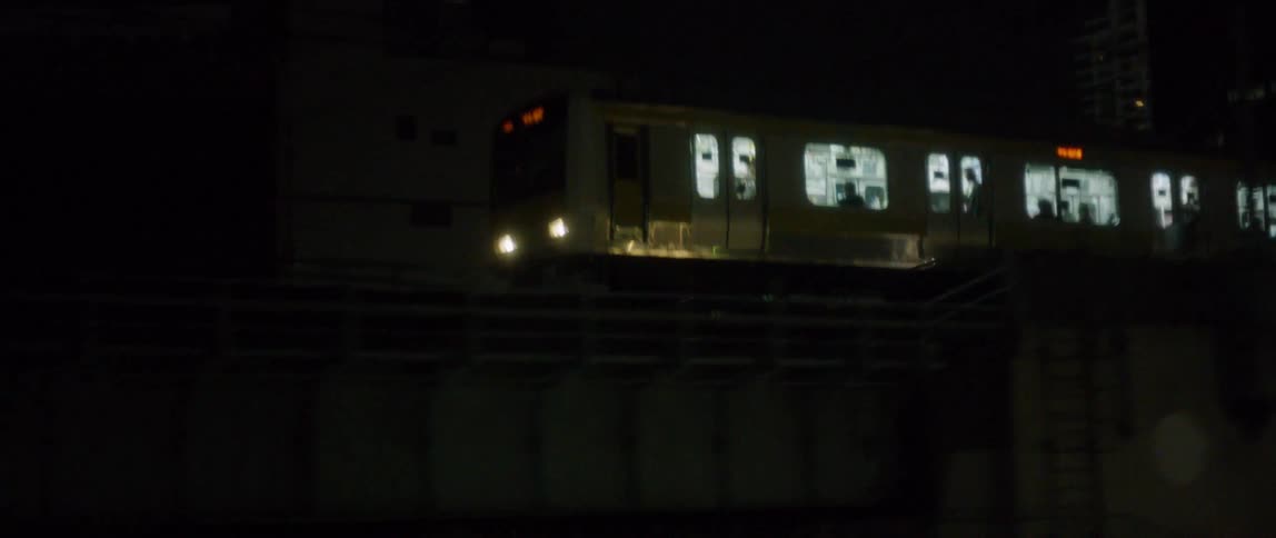 A commuter train is traveling on an elevated track in a city at night