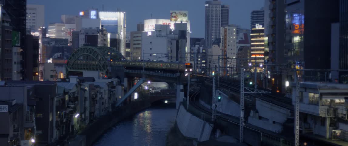 A commuter train is traveling on an elevated track in a city at dusk