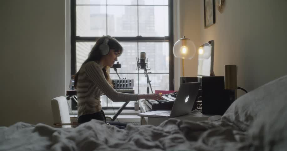 A woman wearing headphones plays a keyboard in her apartment