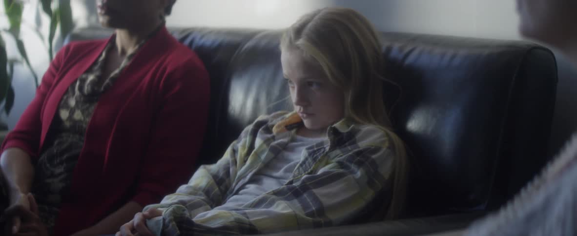 A young, blonde girl sitting next to a black woman on a couch