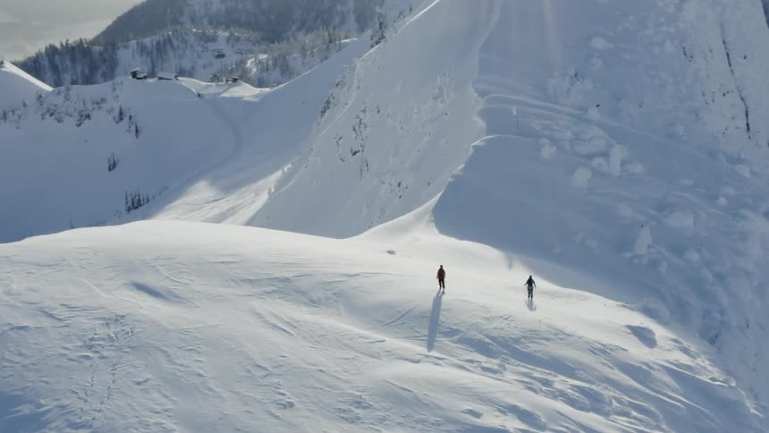 Two people snowboard down a snowy mountain