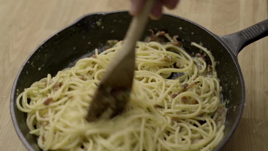 Pasta is tossed in a pan with a wooden spoon