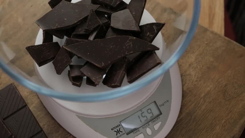 Pieces of broken chocolate being poured into a bowl on a measuring scale