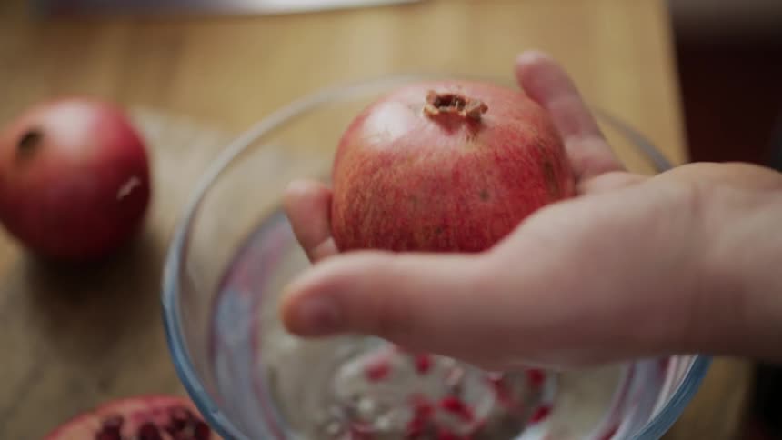 A woman holding half a pomegranate in her hand as she hits the top with a spoon to release the seeds