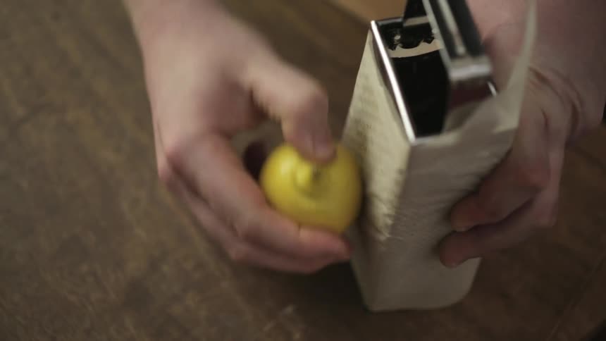 Person wrapping paper around a grater and grates a lemon