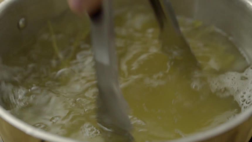 Man using tongs to toss pasta cooking in boiling water