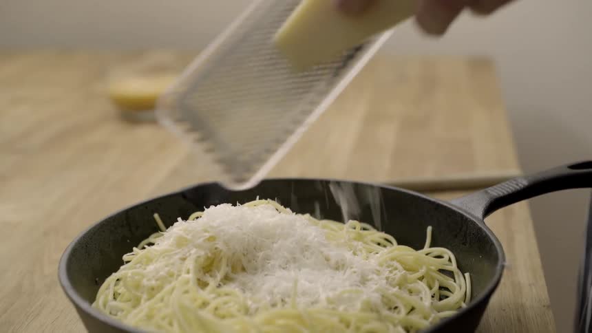 Cheese being grated onto a saucepan of pasta