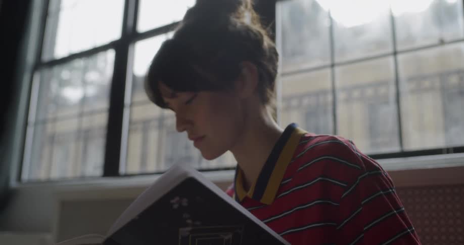 A woman is sitting on the floor of her apartment writing in a notebook during the day