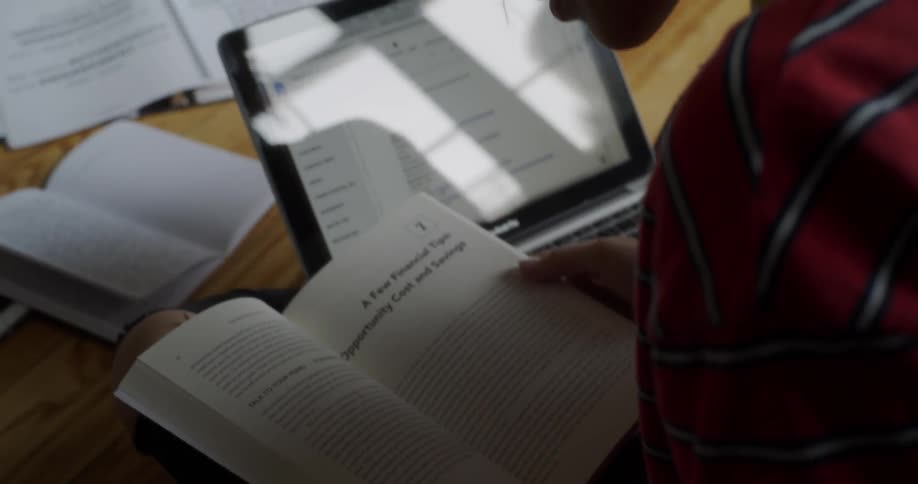 A woman is sitting on the floor flipping through a book as she studies during the day