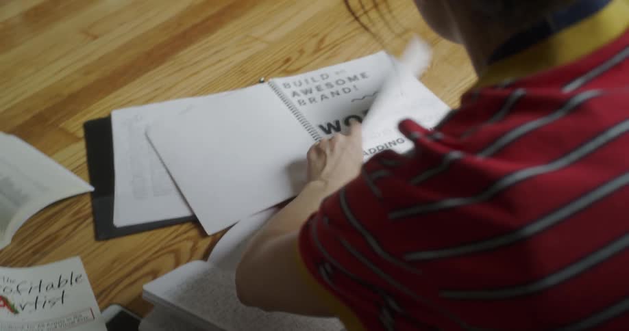 A woman is flipping through a workbook as she sits on the floor in daylight