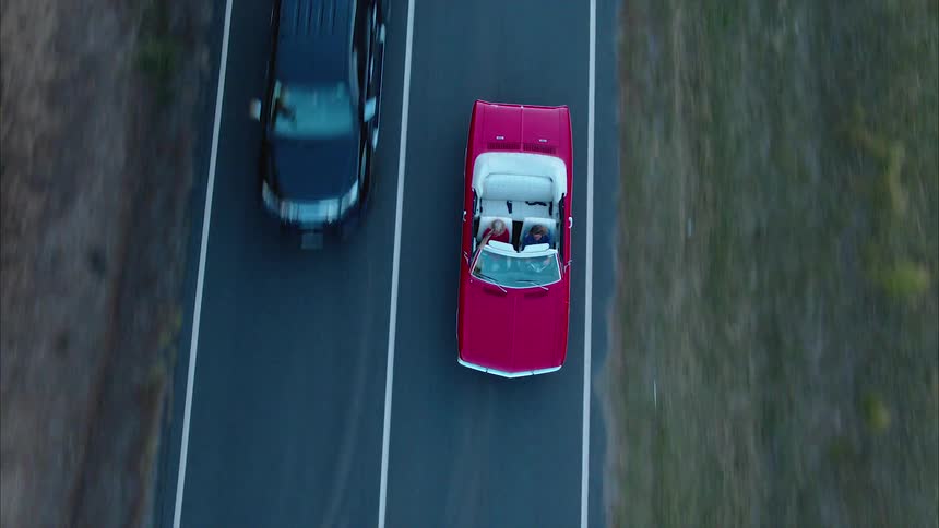 A red convertible with two people drive down the road