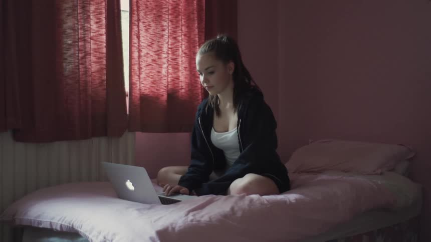 Teenage girl sitting on her bed looking at her laptop