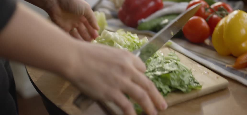A person is cutting lettuce and placing it in a bowl inside a kitchen in daylight