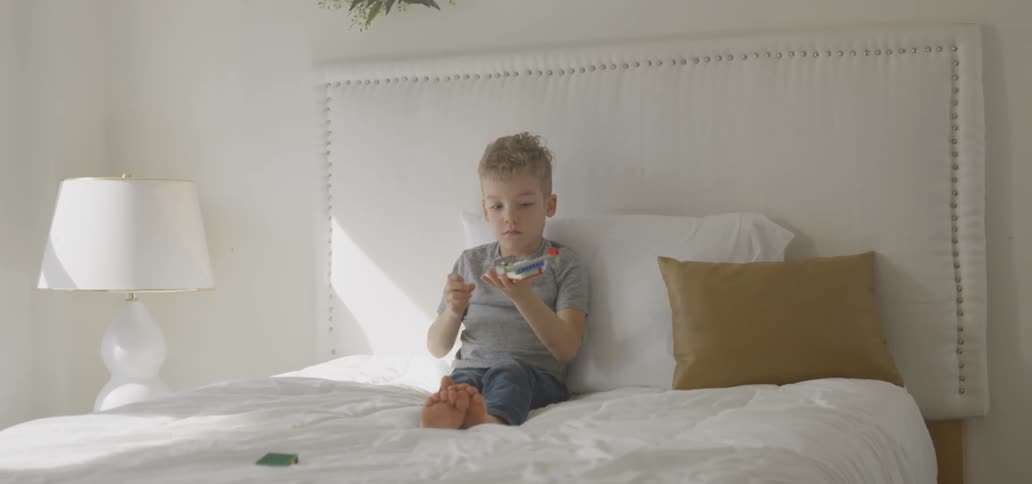 A young boy plays with legos on a bed