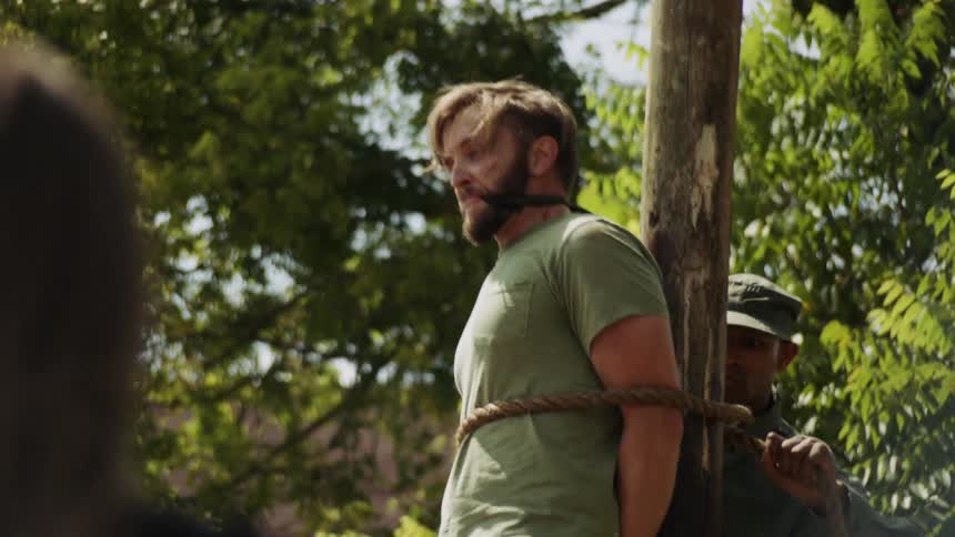 Soldier ties a prisoner to a wood pole