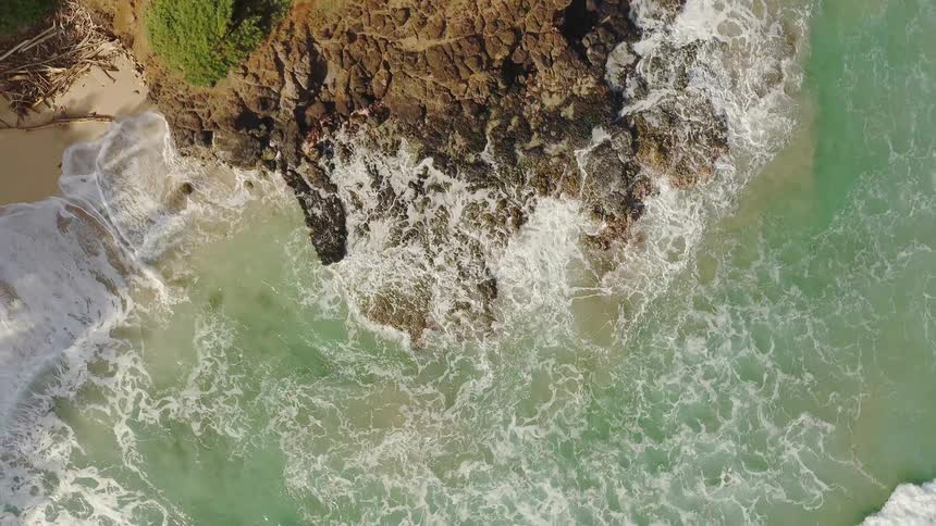 Waves are crashing against rocks on a beach during the day