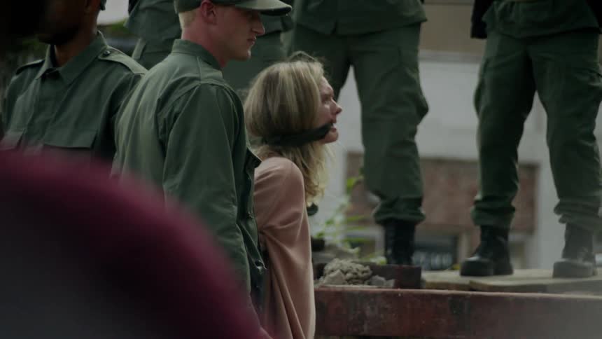 Soldiers aim guns while a gagged woman cries