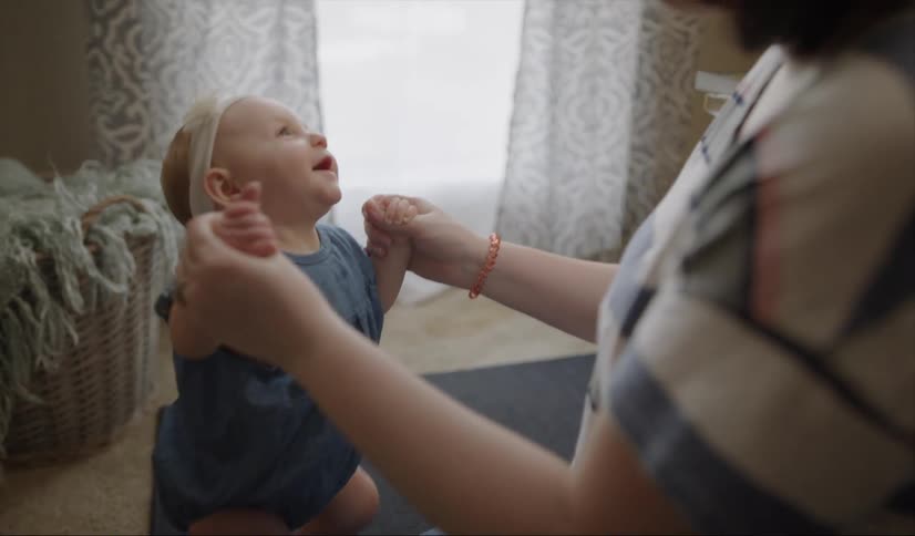 A woman is holding her baby in a standing position as they play inside in daylight