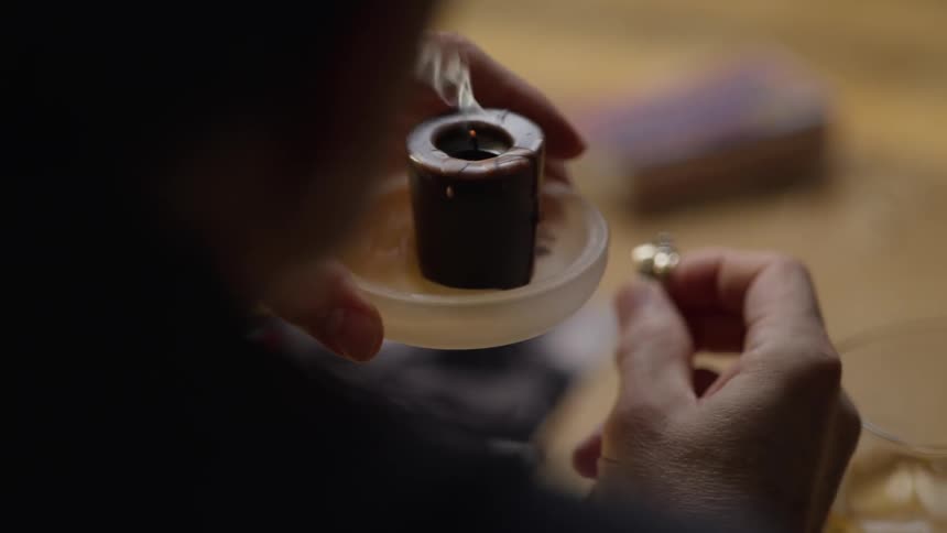 Person sitting at a table holding a ring and blowing out a candle