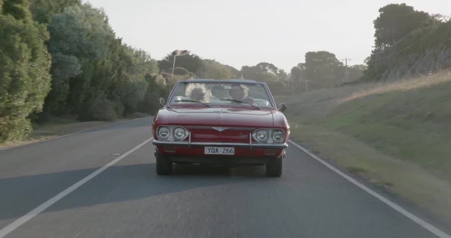 A convertible car is driven on a rural road