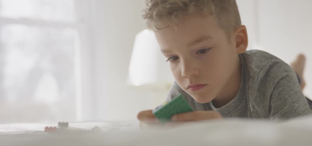 A boy plays with legos on a bed on a sunny day