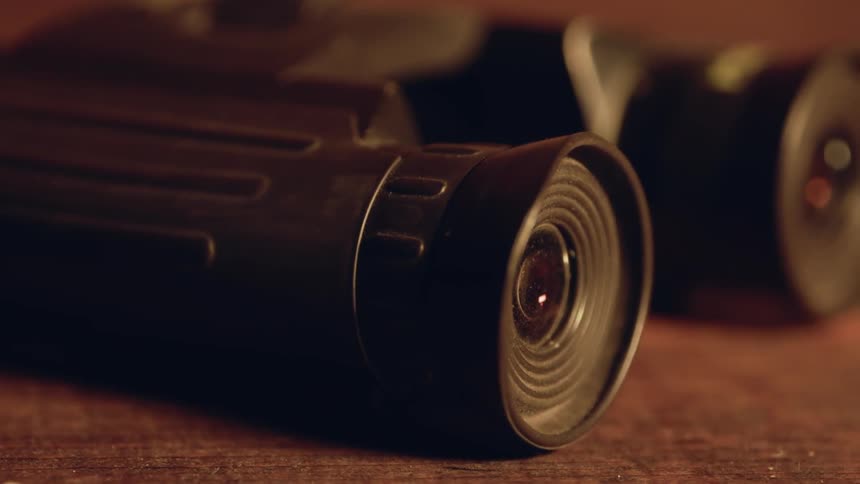 A pair of binoculars are sitting idle on a table in daylight